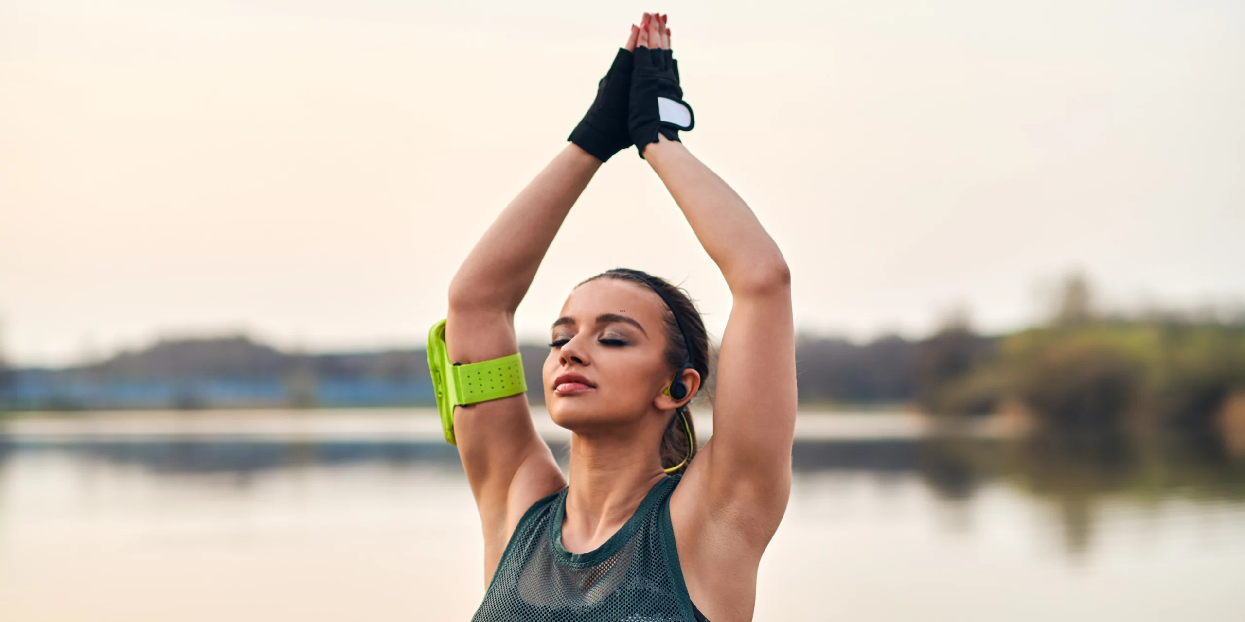  Jeune femme faisant un étirement bras levés, en tenue de sport, au bord de l’eau.