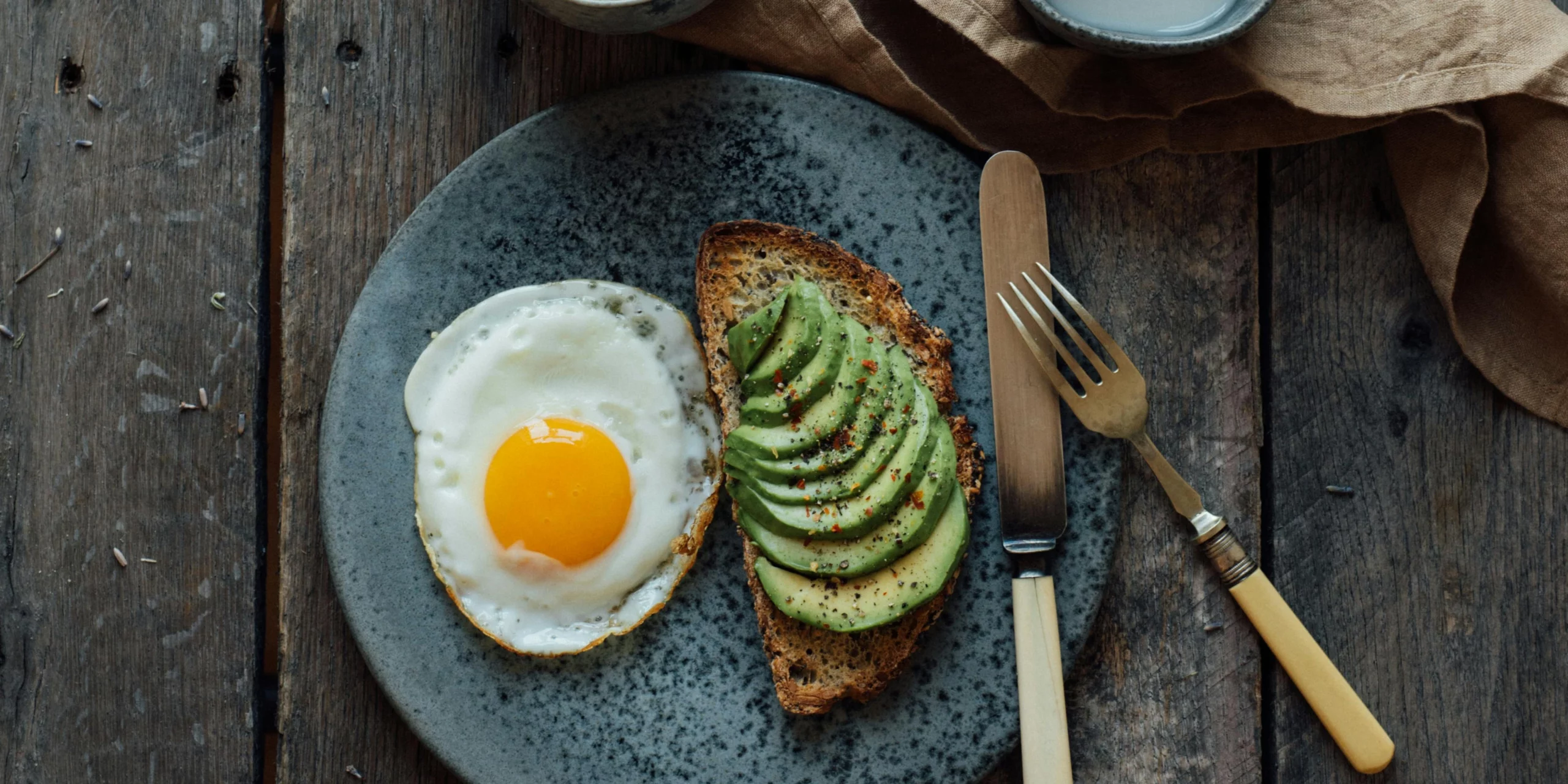 Une tartine à l'avocat et un œuf au plat présentés sur une assiette en céramique, pour un petit-déjeuner sous le signe de l'équilibre et de la douceur.