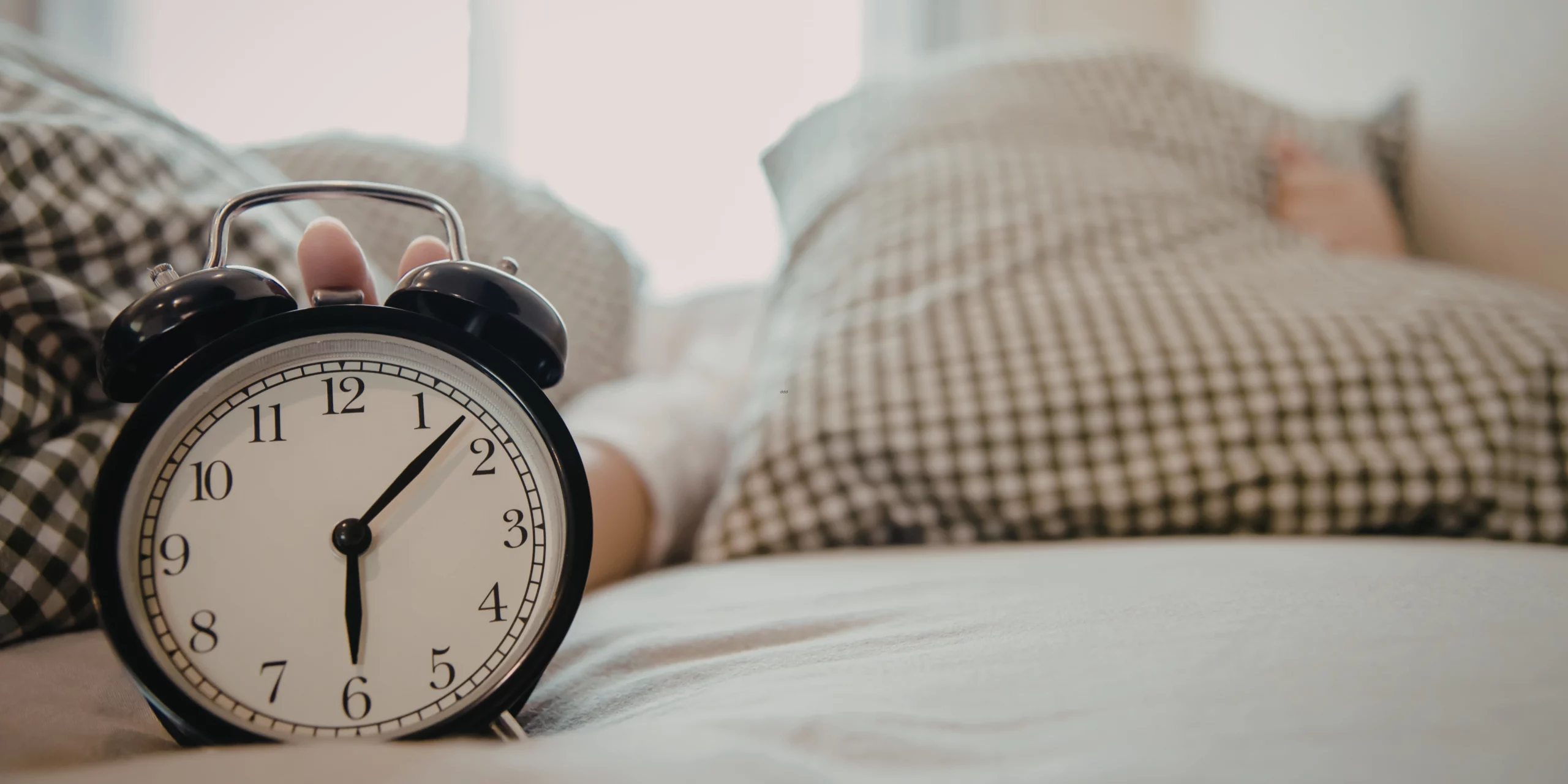 Une main tenant un réveil sur le lit.